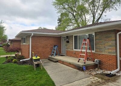 Progress photo of a Michigan brick home during installation of a white aluminum awning with red trim by Wayne Craft