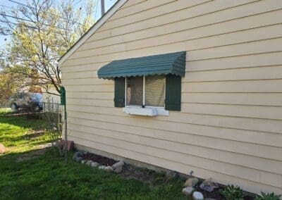 Side view of a Michigan home featuring a green aluminum window awning built by Wayne Craft